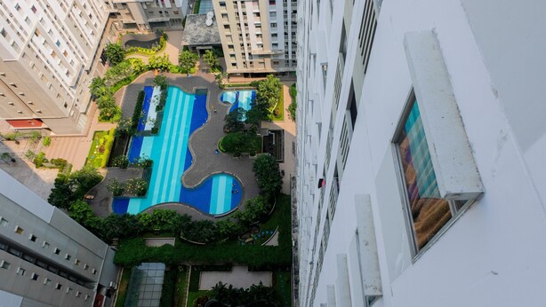 An aerial view of a residential building complex with a swimming pool, green spaces, and a modern architectural design.