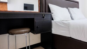 A neatly arranged hotel room with a bed, a small desk with a chair, and a bedside table.