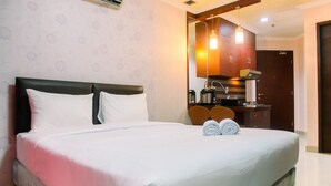 Una habitación de hotel con una cama grande, un escritorio con silla, un espejo y una kitchenette.