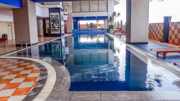 Una piscina con un piso de patrón a cuadros, pared de azulejos y vista al exterior.