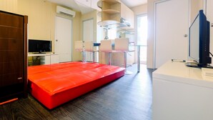 Ein modernes Hotelzimmer mit einem roten Sofa, einem Schreibtisch mit einem Computer und einem Fernseher.