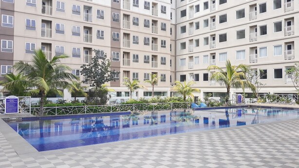 Een meerlaags hotel met een zwembad, palmbomen en een geruit vloerkleed rondom het zwembad.