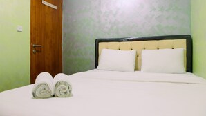 Een net opgemaakt bed met witte lakens en twee opgerolde handdoeken aan het voeteneind.