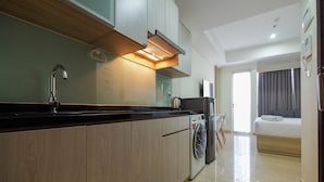 Una cucina moderna con lavatrice integrata, una zona pranzo con tavolo e sedie, e una camera da letto con un letto e tende.