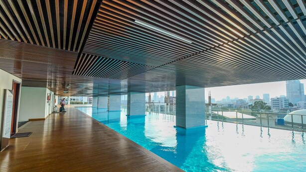 Una piscina interna moderna con pavimento in legno e soffitto a listelli, affacciata su una vista urbana.