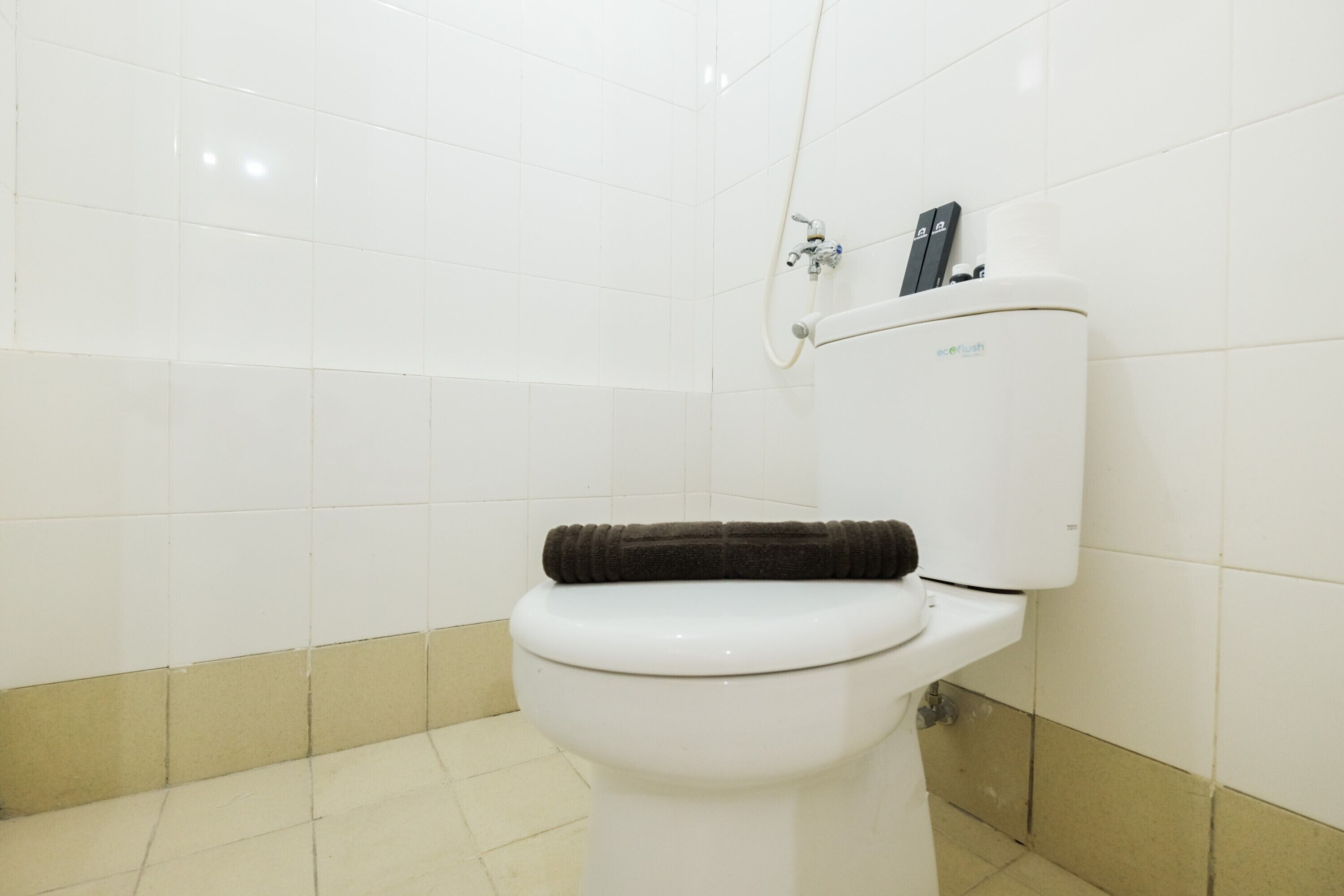 A white toilet with a brown towel on the seat, a flush handle, and a bidet attachment on the wall.