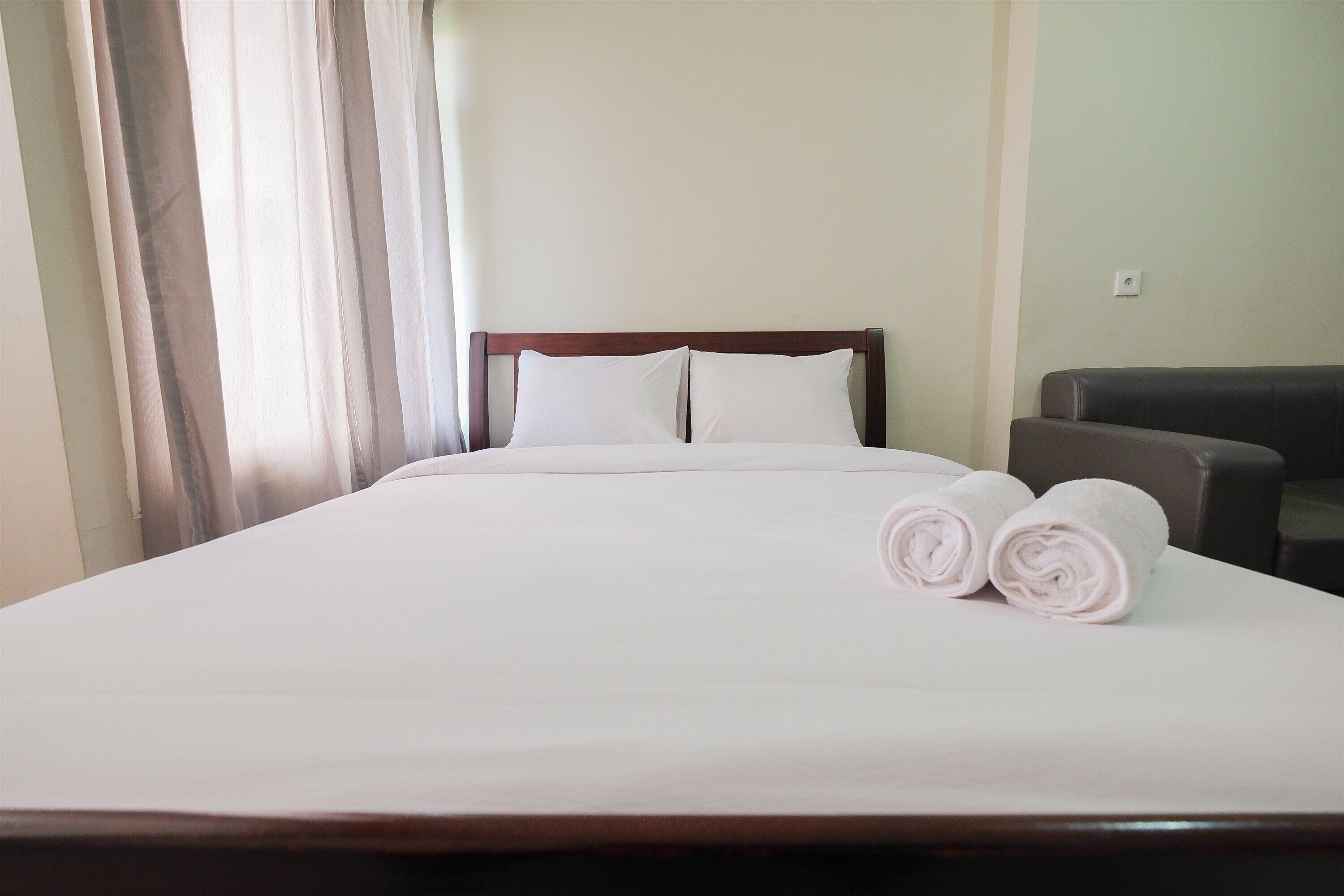 A neatly made bed with white linens and two rolled towels on the side.