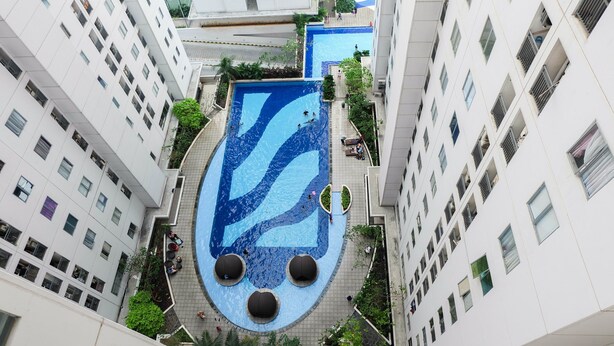 Un edificio de gran altura con piscina en la azotea y vegetación circundante.