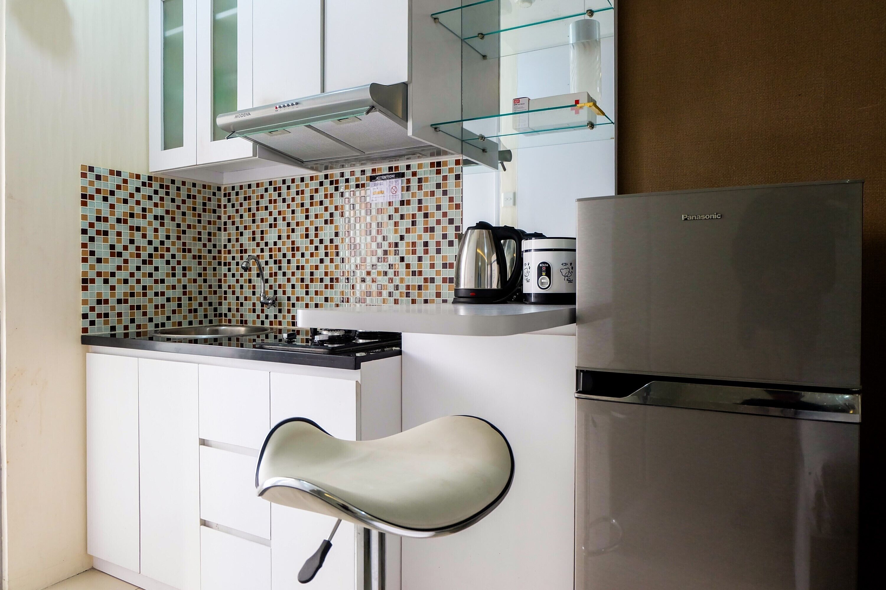 A compact kitchen with a modern stove, a stainless steel refrigerator, and a unique bar stool.