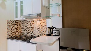 Una cocina moderna con armarios blancos, salpicadero de azulejos, pileta de acero inoxidable, hervidor, cocedora de arroz y refrigerador.