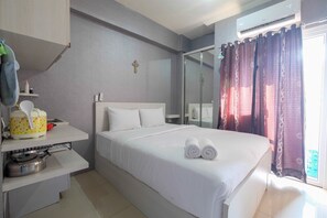 A hotel room with a bed, a small table with a kettle, a shelf with toiletries, and a window with curtains. - Mini Studio Green Pramuka Apartment (Jakarta)