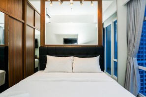 A hotel room with a large bed, wooden wardrobe, and a view of a cityscape through the window.