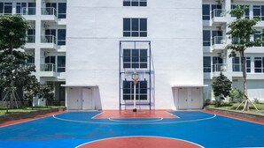 Una cancha de baloncesto con superficie azul y roja, rodeada por un edificio blanco con varias ventanas y balcones.