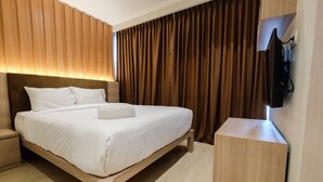 A modern hotel room with a wooden bed, a bedside table, and a wall-mounted TV. - Comfortable and Modern 2BR Menteng Park Apartment (Jakarta)