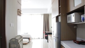 A modern hotel room with a bed, a desk, a microwave, and a refrigerator. - Comfortable Studio at Beverly Dago Apartment near ITB (Bandung)