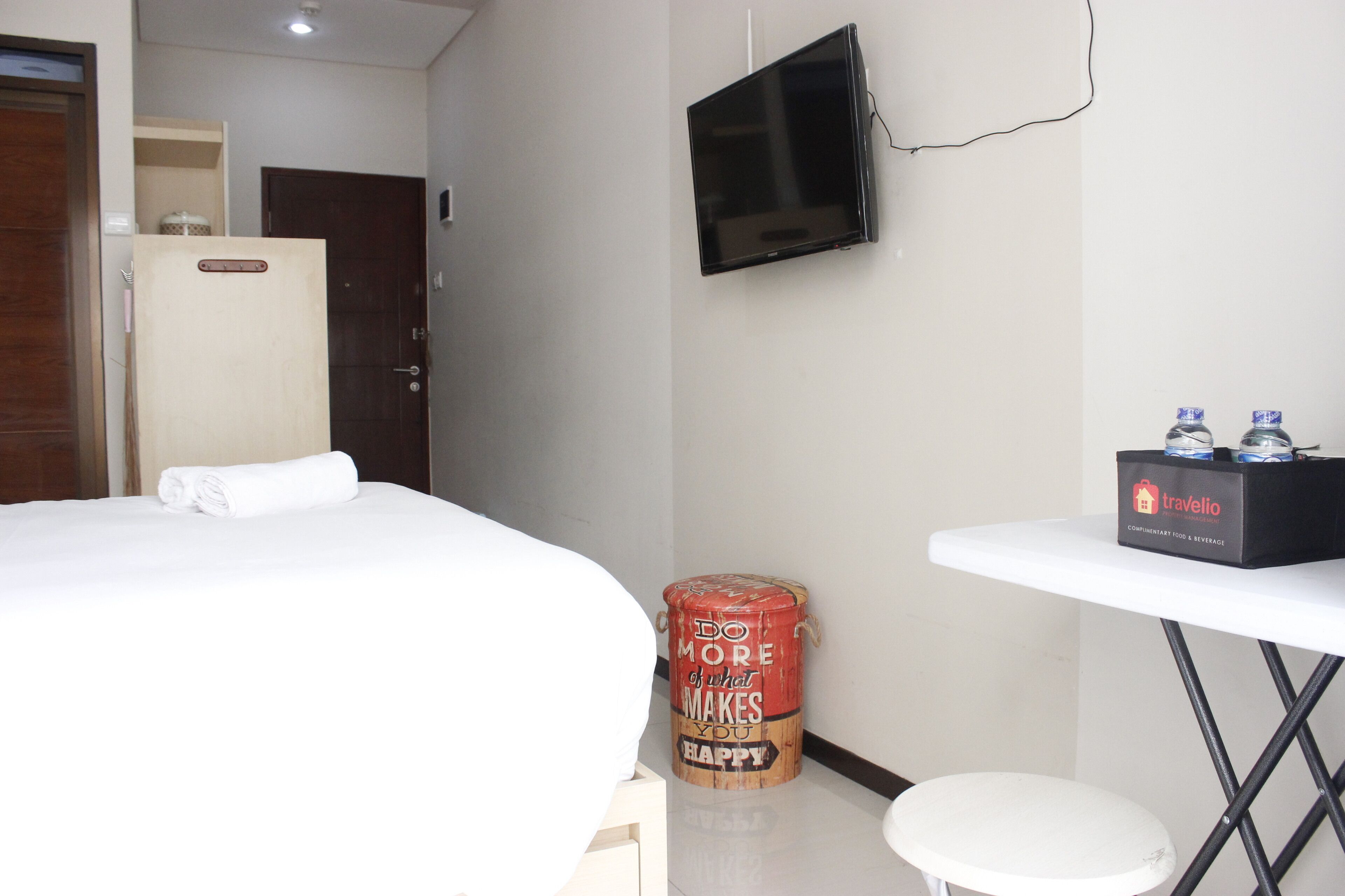 A hotel room with a bed, a small table with bottled water, a television, and a motivational quote on a container.