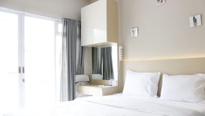 A hotel room with a bed, a desk, a chair, a mirror, and a window with curtains. - Homey Studio Gateway Pasteur Apartment near Exit Toll (Cimahi)