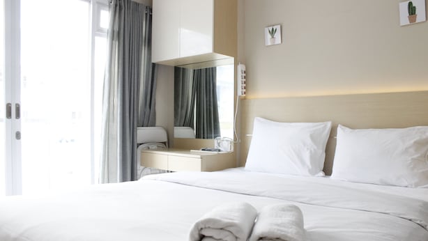 A hotel room with a neatly made bed, a bedside table with a lamp, and a window with curtains. - Homey Studio Gateway Pasteur Apartment near Exit Toll (Cimahi)