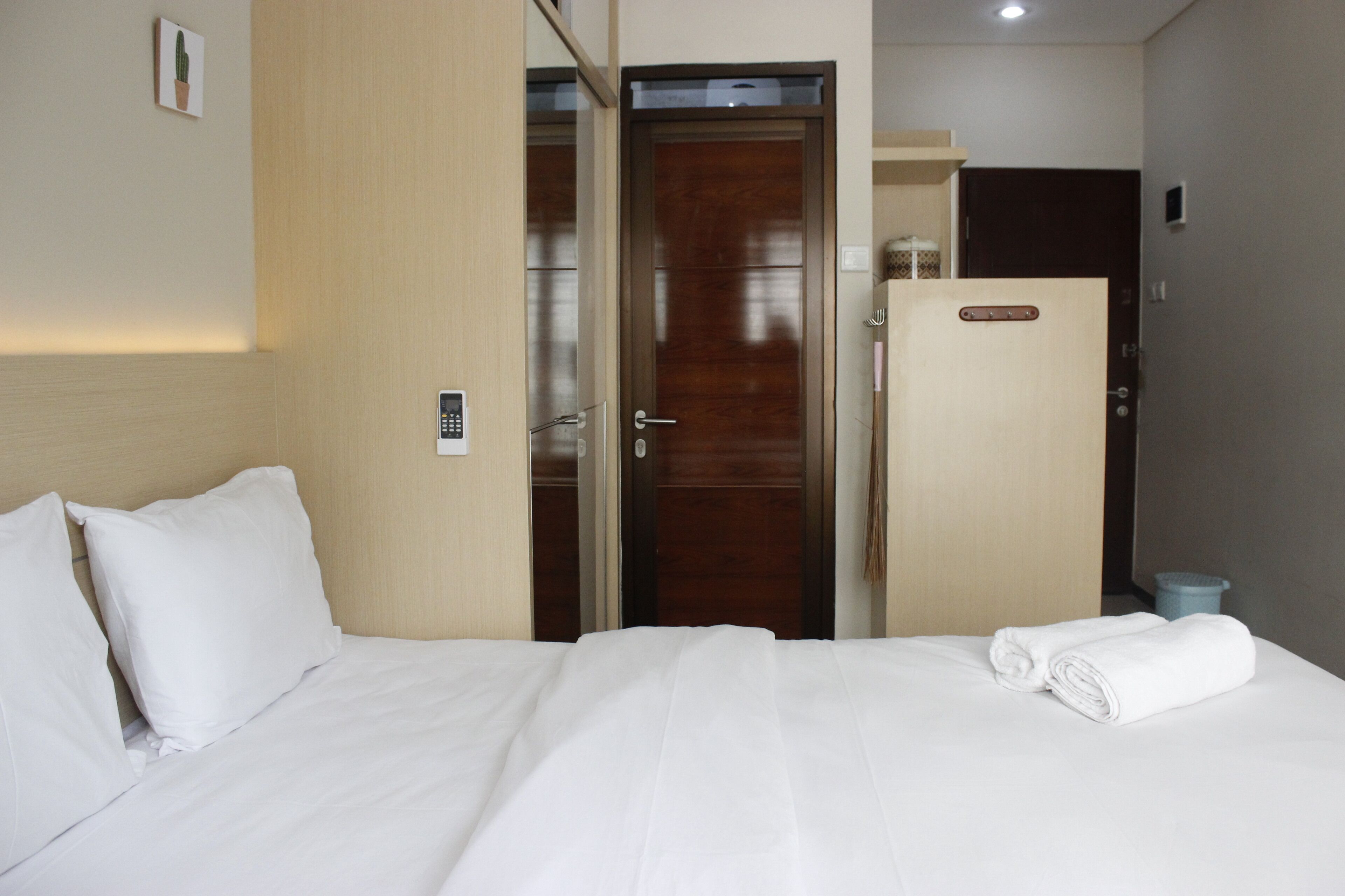Habitación de hotel con cama, puerta de madera, un cubo de basura pequeño y una lámpara fijada a la pared.