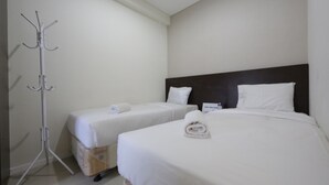 A hotel room with two single beds, a dark headboard, and a coat rack. - Clean and Cozy 2BR Apartment @ Parahyangan Residence (Bandung)