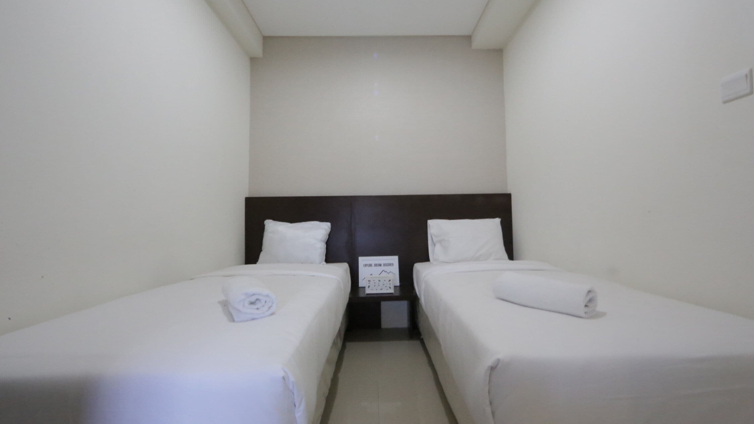A small, clean room with two single beds, a dark headboard, and a sign on the wall.