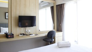 Ein Hotelzimmer mit einem Bett, einem Schreibtisch mit Stuhl, einem Fernseher und einem Fenster mit Vorhängen.