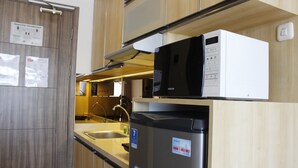 Eine kleine Küche mit Holzschränken, einem Edelstahlkühlschrank, einer Mikrowelle und einem Spülbecken.