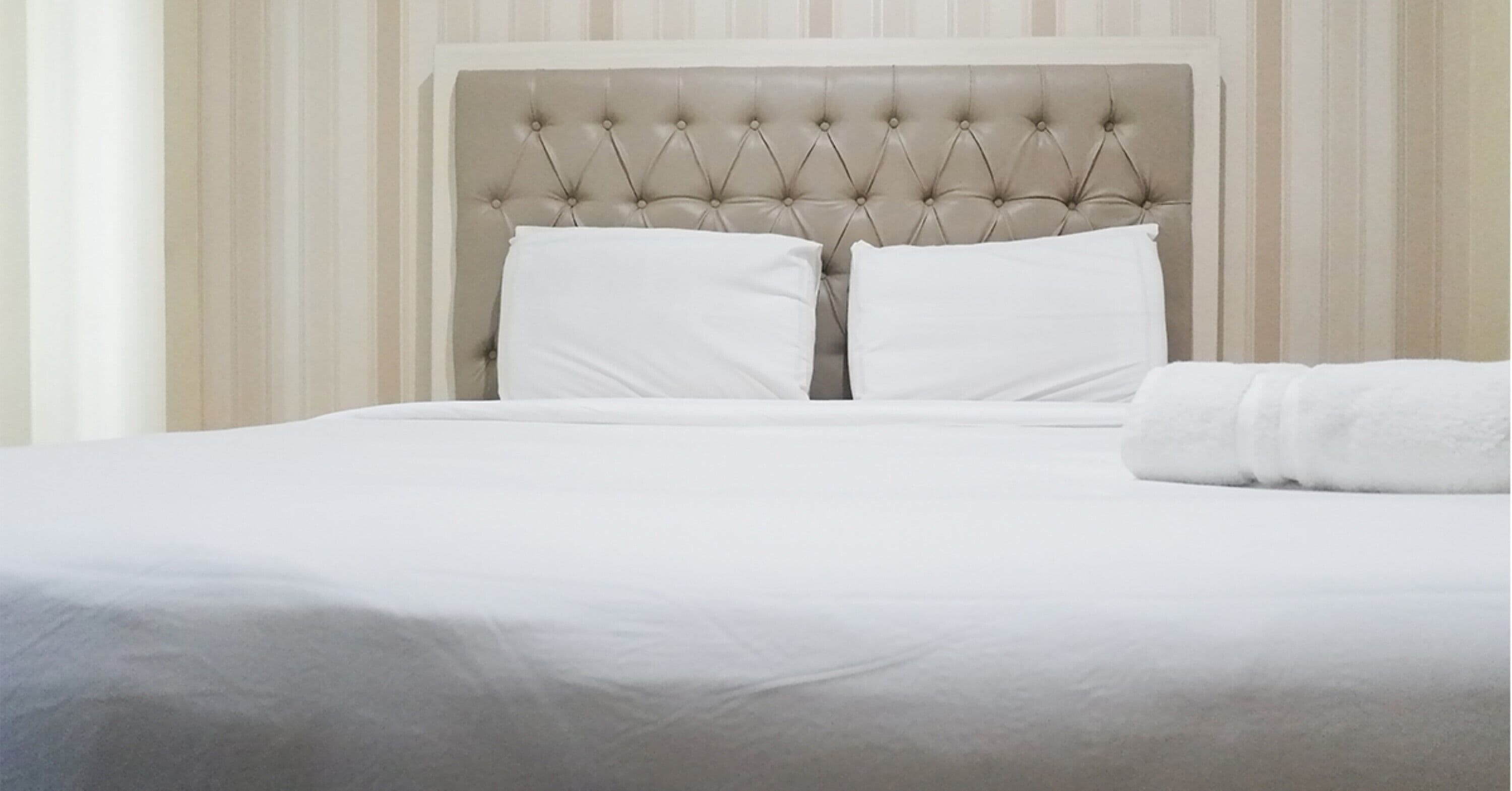 A neatly made bed with white linens and a tufted headboard.