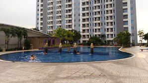 Une piscine avec une terrasse carrelée, entourée de palmiers et, au fond, un grand immeuble d’habitation.