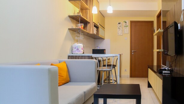 A living room with a sofa, a coffee table, and a dining area with a table and chairs. There is a kitchen area with a refrigerator and a microwave.