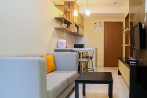 A living room with a sofa, a coffee table, and a dining area with a table and chairs. There is a kitchen area with a refrigerator and a microwave. - Modern 1BR with Sofa Bed @ Cinere Bellevue Apartment (Depok)