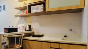 A kitchen with a microwave, coffee maker, and a sink. There are wooden cabinets and a bar stool.