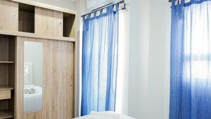 A hotel room with a bed, a mirror, a wardrobe, and blue curtains. - Modern Living 1BR @Atlanta Residences Apartment With City View (Depok)