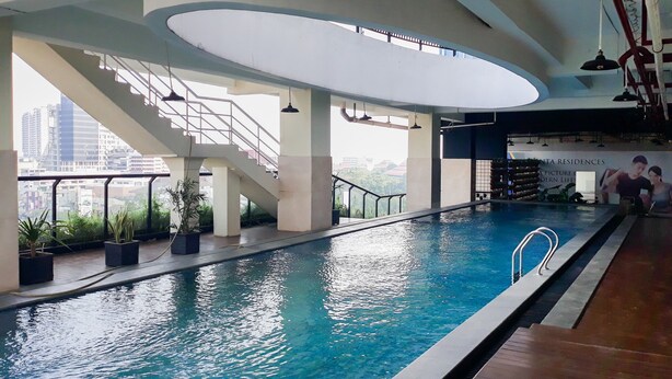 An indoor swimming pool with clear blue water, surrounded by a modern architectural design with large windows and potted plants. - Modern Living 1BR @Atlanta Residences Apartment With City View (Depok)