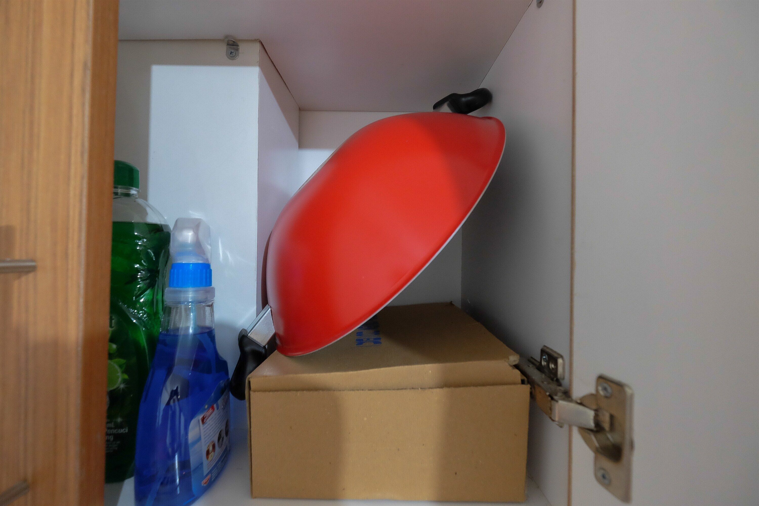Un pequeño espacio de almacenamiento con una caja de cartón, una palangana de plástico rojo y una botella de líquido azul.