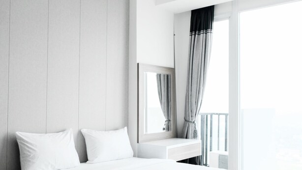 A modern hotel room with a large bed, a bedside table, a mirror, and a window with curtains. - Homey Studio Room Tree Park Apartment near BSD City (South Tangerang)