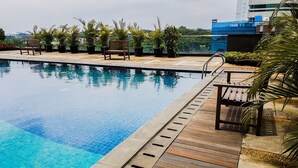 A swimming pool with wooden deck and potted plants, surrounded by buildings. - Homey Studio Room Tree Park Apartment near BSD City (South Tangerang)