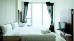 A hotel room with a large bed, a TV mounted on the wall, and a balcony with curtains. - Homey Studio Room Tree Park Apartment near BSD City (South Tangerang)