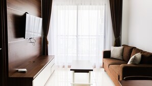 A modern hotel room with a wooden TV stand, a flat-screen TV, a brown sofa, and a white coffee table.