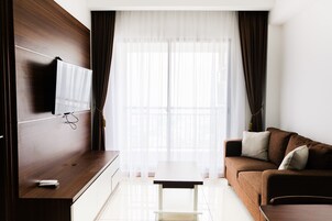 A modern hotel room with a wooden TV stand, a flat-screen TV, a brown sofa, and a white coffee table.