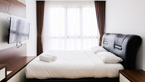A hotel room with a bed, a flat-screen TV mounted on the wall, and a window with curtains.