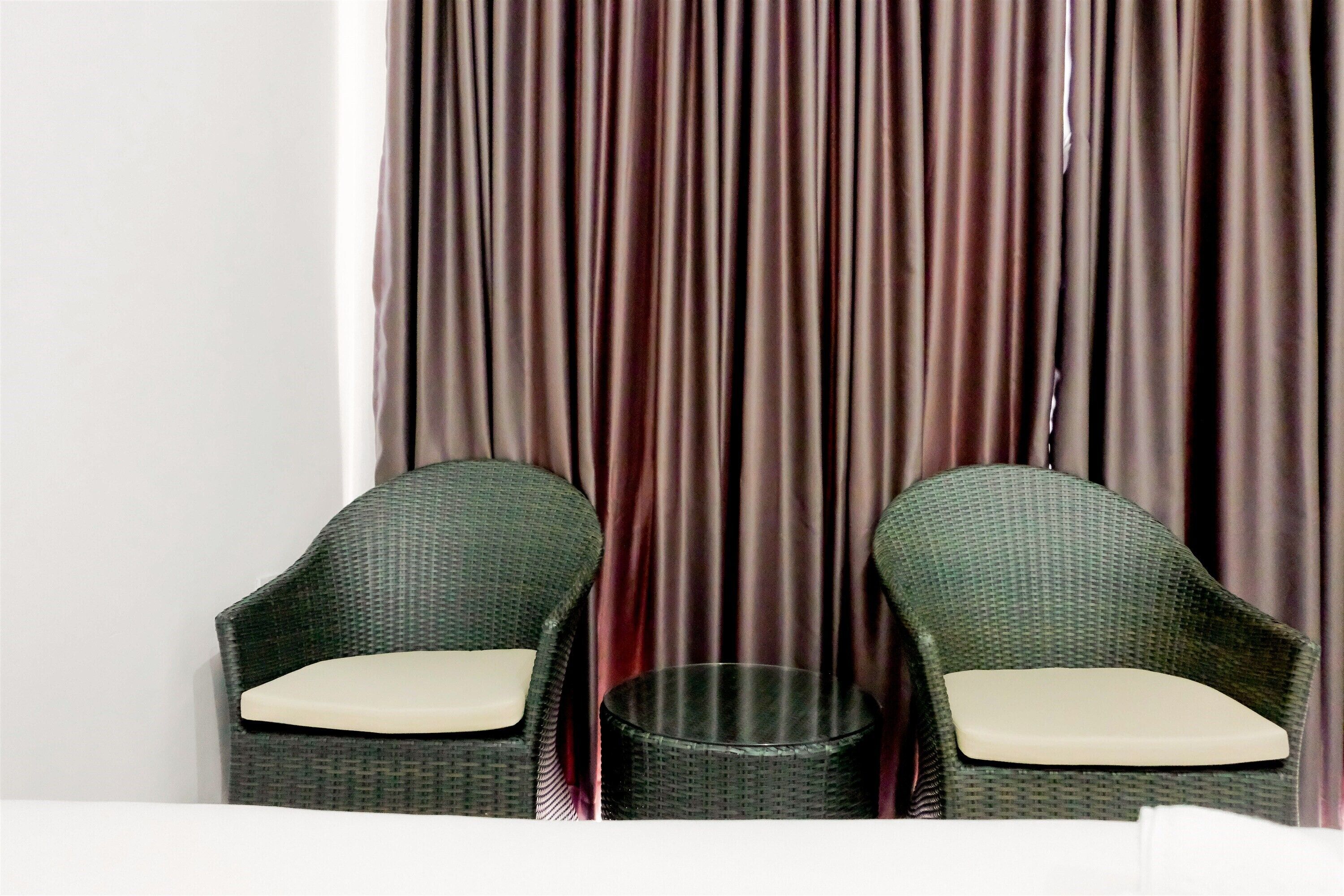 Two wicker chairs with beige cushions in front of a curtain.