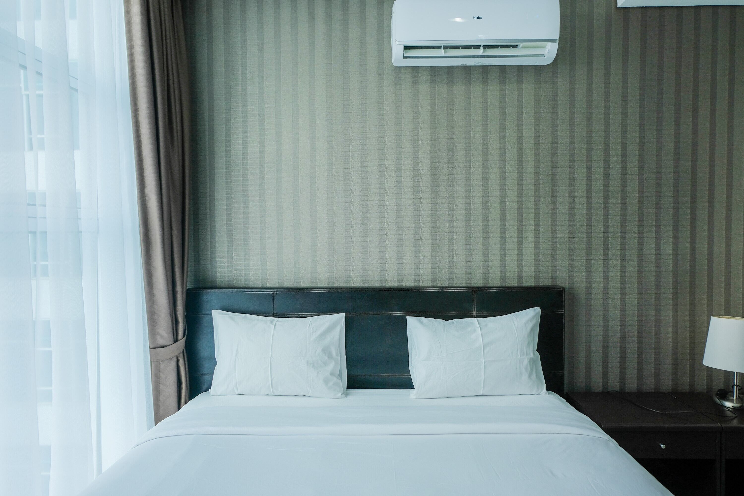 Quarto de hotel com cama, mesa de cabeceira, luminária e ar condicionado fixado na parede.