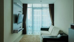 A modern hotel room with a flat-screen TV mounted on a wall, a sofa, and a large window with curtains. - Stylish 2BR at Brooklyn Apartment near Alam Sutera (South Tangerang)