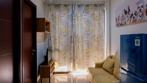 Una sala de estar con un sofá, un televisor, un mueble de madera y un refrigerador.