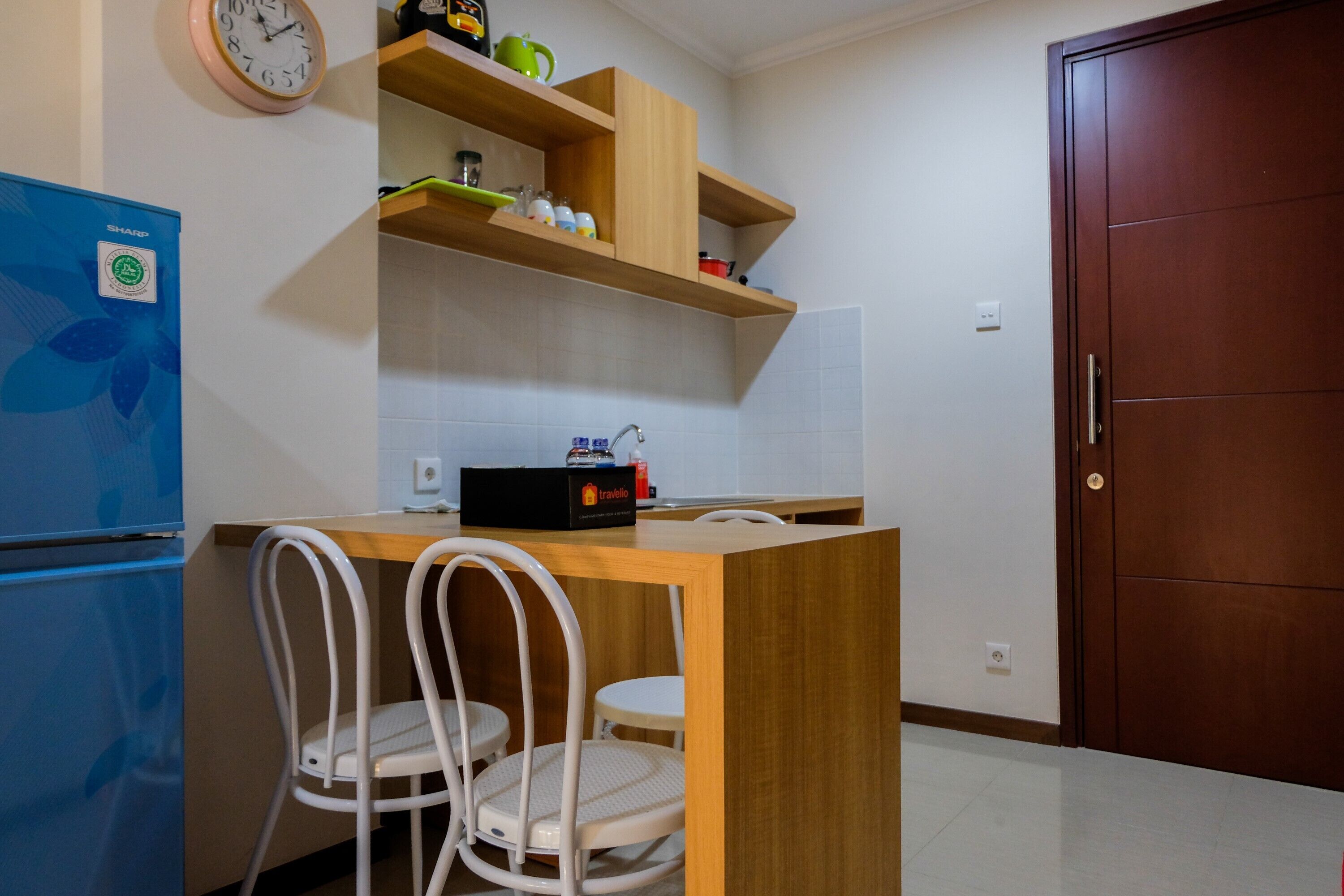 A compact kitchen with a wooden countertop, two white chairs, a blue refrigerator, and a wooden door.