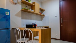 Una cocina compacta con encimera de madera, dos sillas blancas, un refrigerador azul y una puerta de madera.