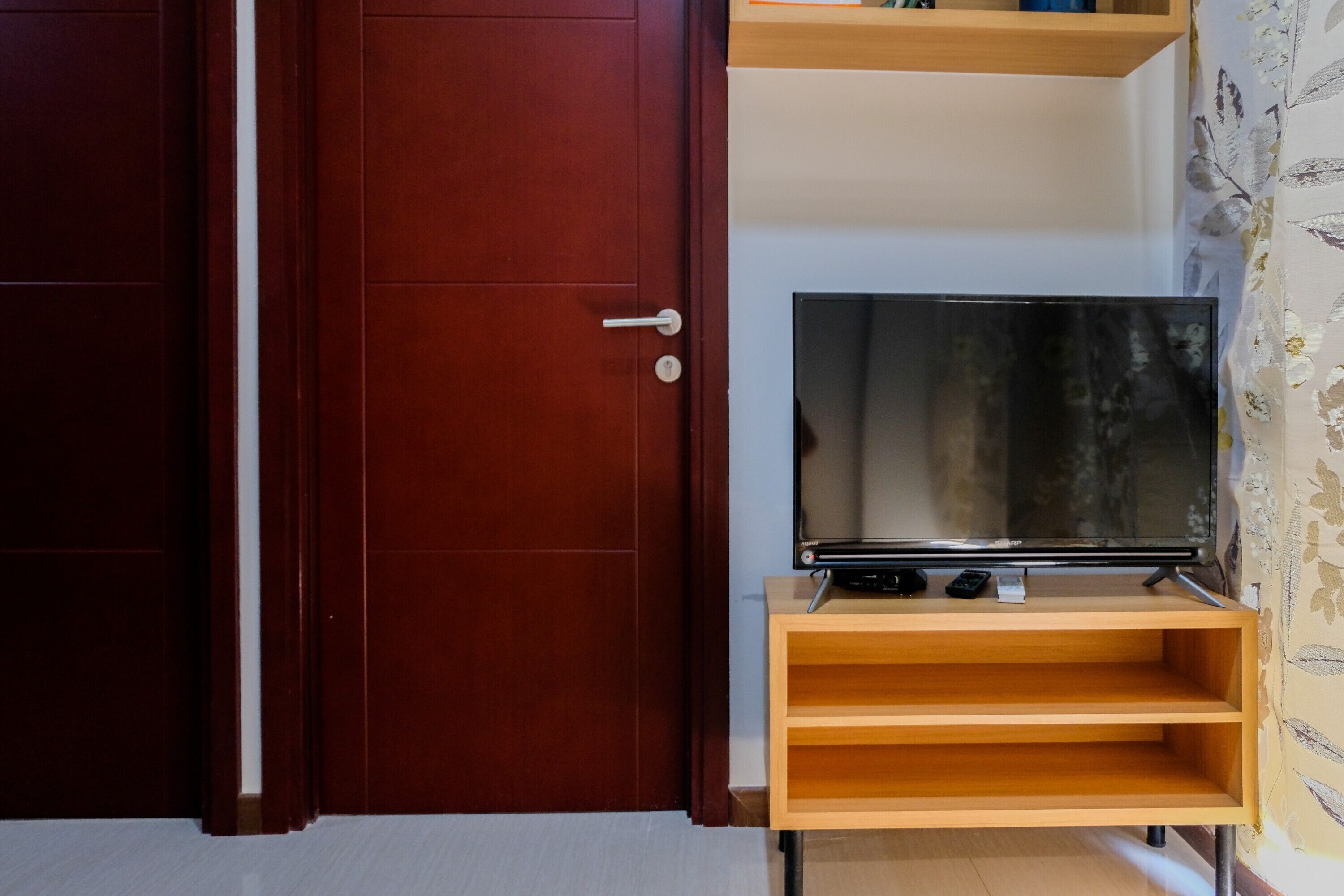 A wooden TV stand with a flat-screen TV, a door with a handle, and a shelf above the TV.