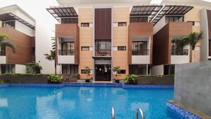 Edificio moderno con piscina central, rodeado de vegetación y con fachadas de ladrillo y azulejos.