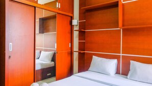 A hotel room with a bed, white linens, a wooden wardrobe, and a mirror. - Highest Value 2BR at Great Western Apartment (Tangerang)